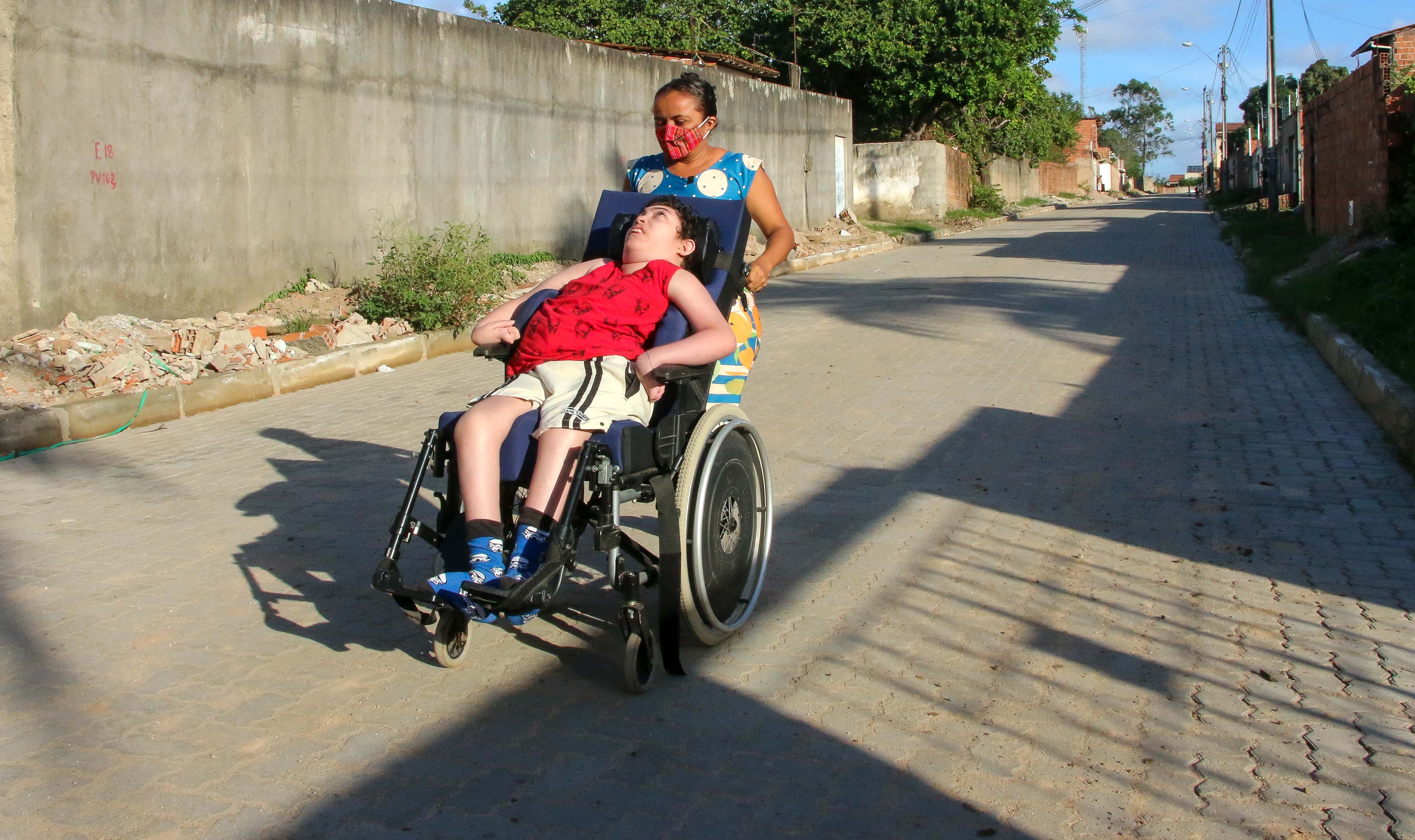Rana empurra a cadeira de rodas do filho Ítalo na rua onde mora